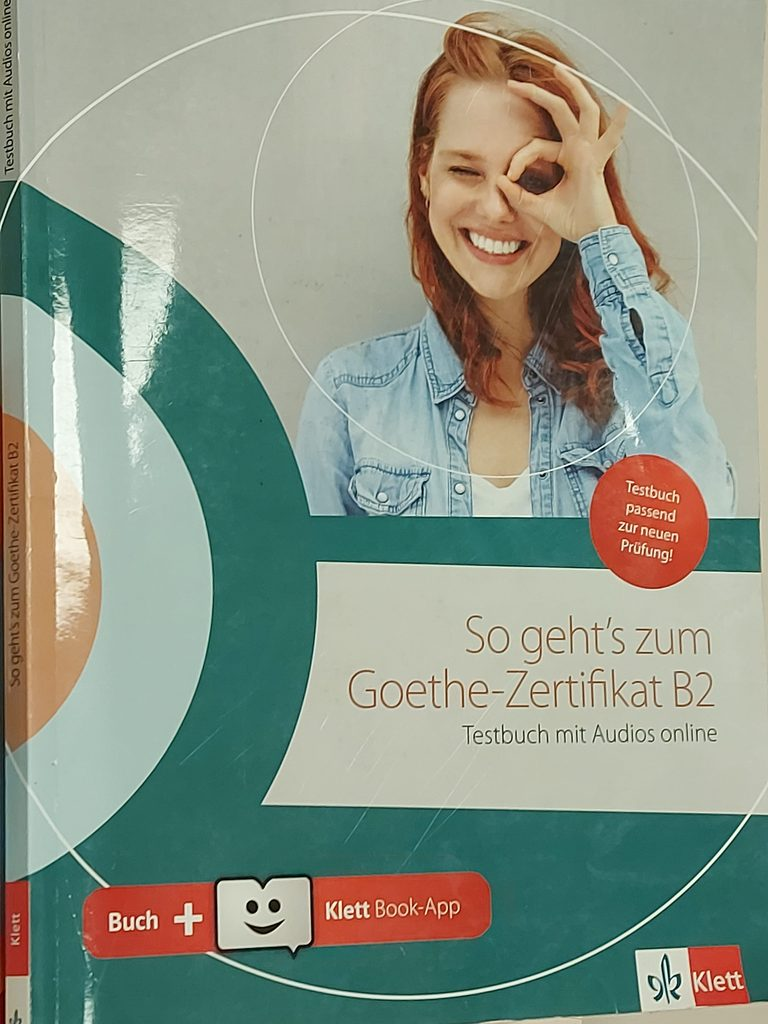 Εξώφυλλο βιβλίου με τίτλο "So geht's zum Goethe-Zertifikat B2", με γυναίκα που χαμογελά και κάνει χειρονομία με το χέρι της.
